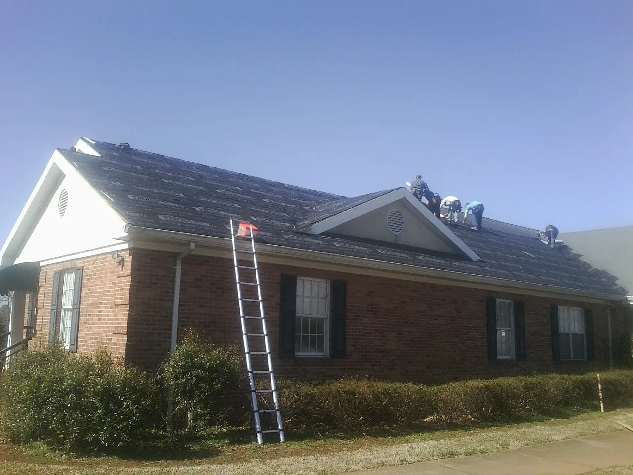 Crew tearing shingles off a brick ranch roof with a ladder set — Emergency Roof Repair work by our crew in Tuckasegee