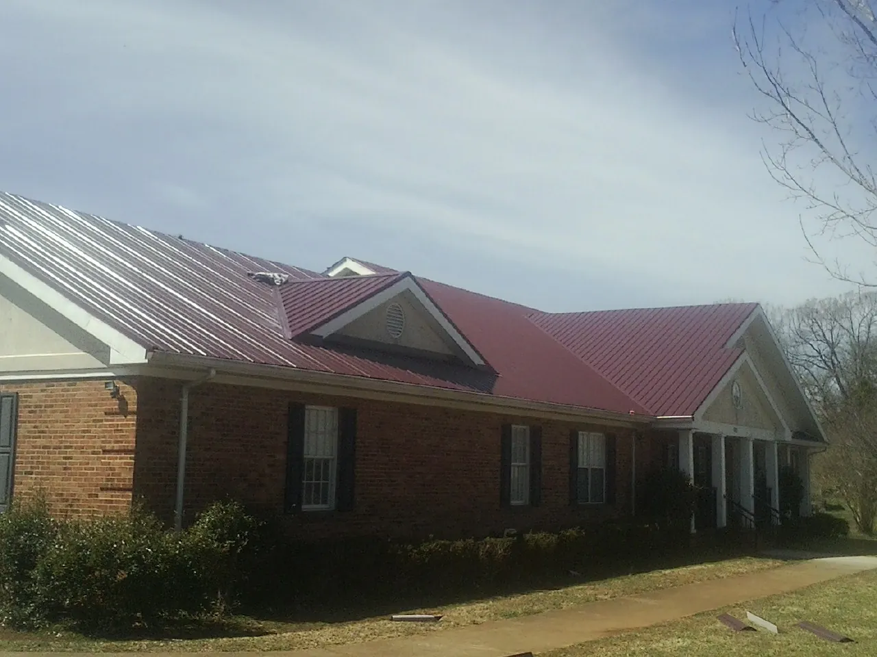 Red metal roof with gabled entries on a long brick building, from a Hail Damage Roof Repair job in Tuckasegee