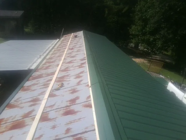 Old rusted panels beside newly installed green metal roofing — Wind Damage Roof Repair by Roofing Brothers in Tuckasegee