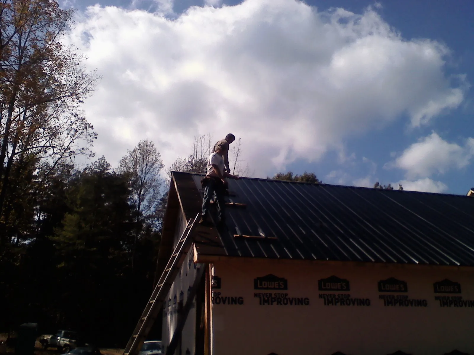 Roofer fastening dark metal panels high against a cloudy sky, from a Roof Inspection job in Tuckasegee