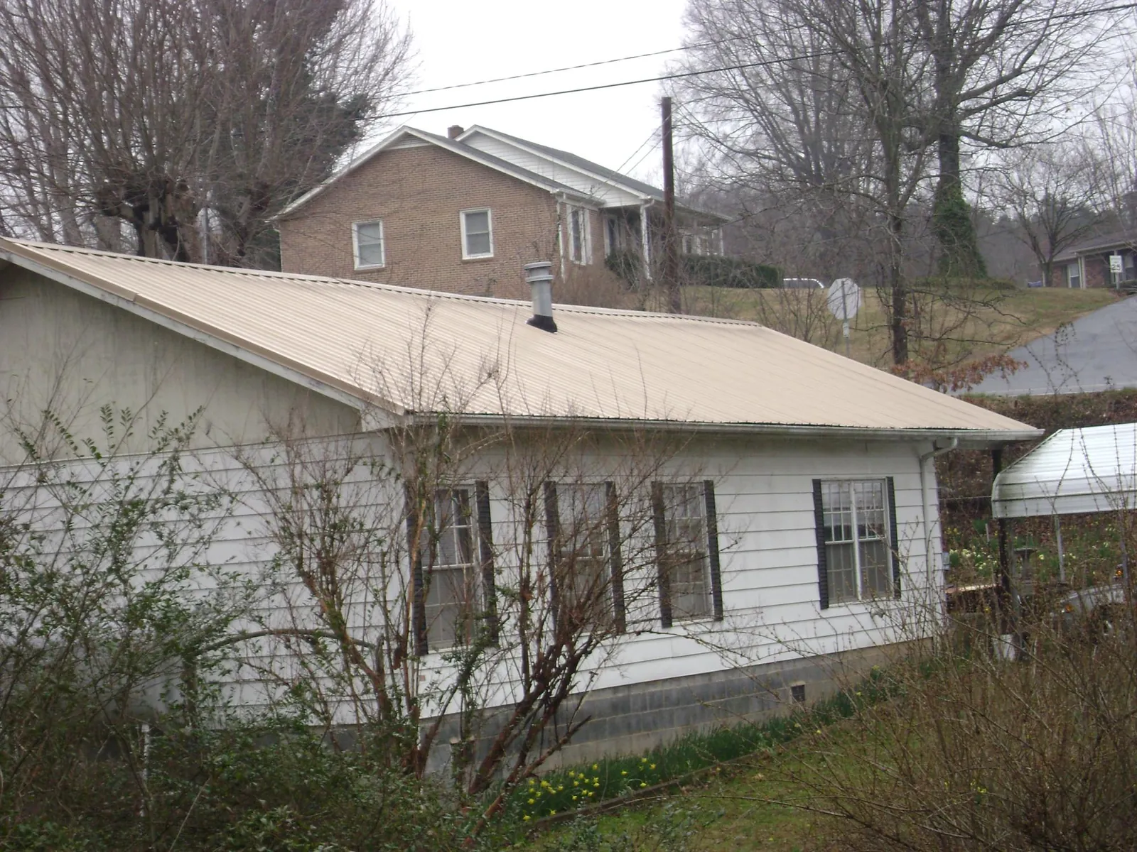 Tan metal roof on a white sided house set into a hillside — Commercial Roofing by Roofing Brothers in Tuckasegee