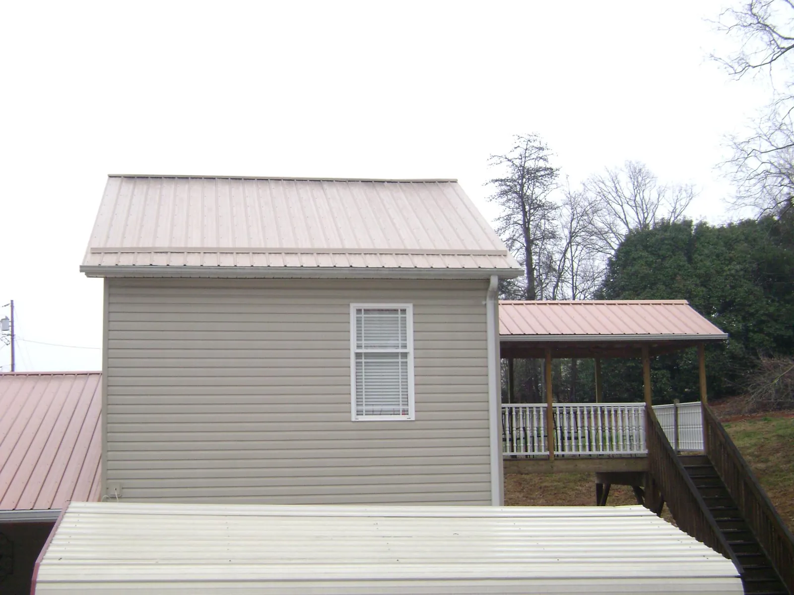 Tan metal roofs on a two story addition and attached porch, from a Roof Replacement job in Tuckasegee